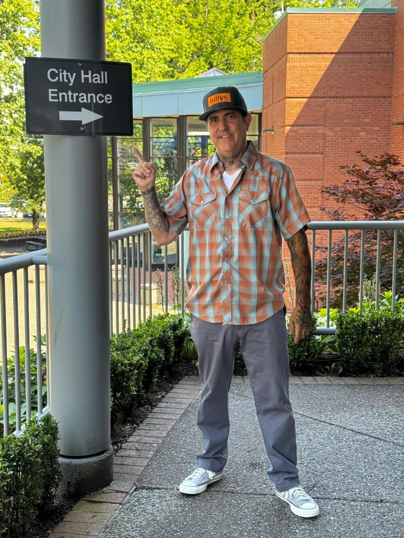 Skully White at Abbotsford City Hall, pointing at the entrance sign.